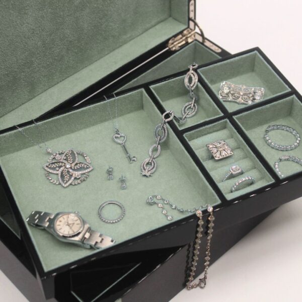 Open black lacquer jewelry box with sage green velvet trays holding diamond and white gold estate pieces