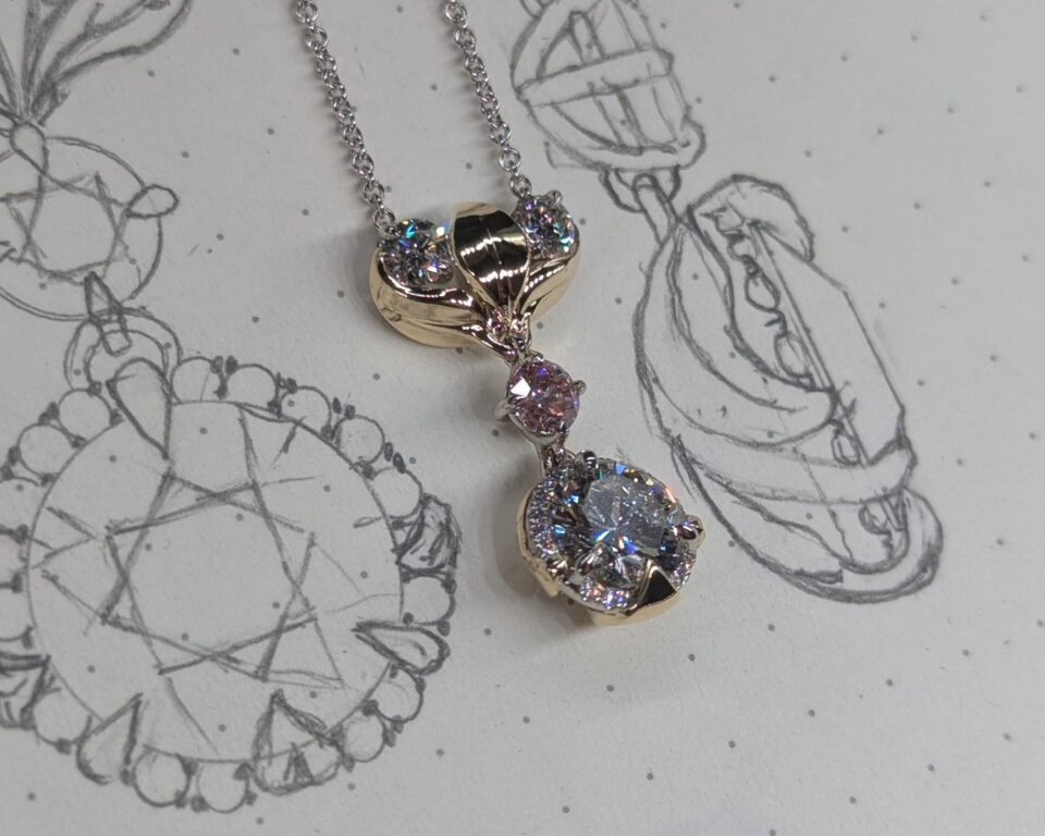 Custom diamond and gold pendant resting on hand-drawn jewelry design sketches at Eco Estate Jewelry