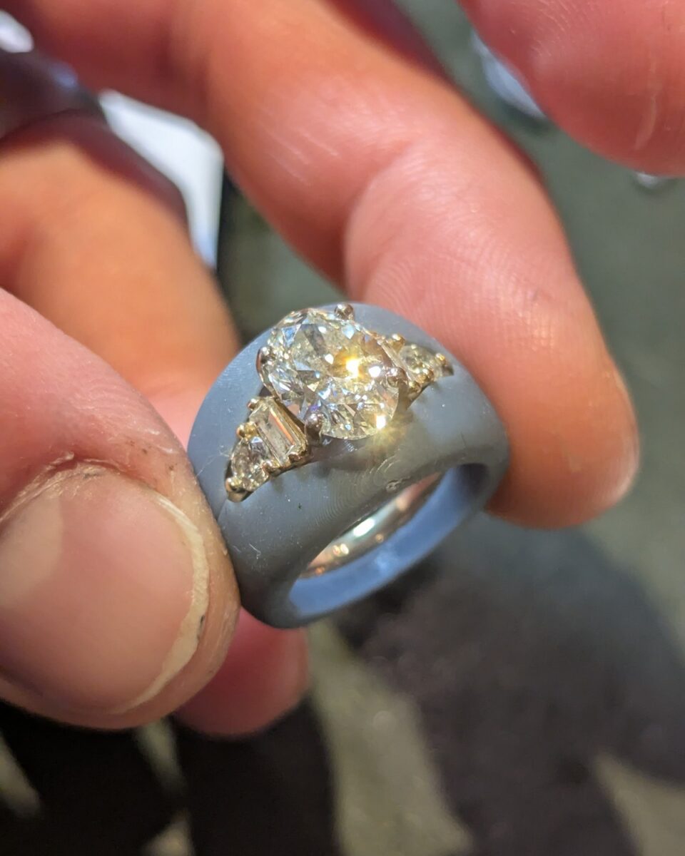Finished custom ring with an oval diamond centre flanked by baguette and trilliant diamonds, held at the bench
