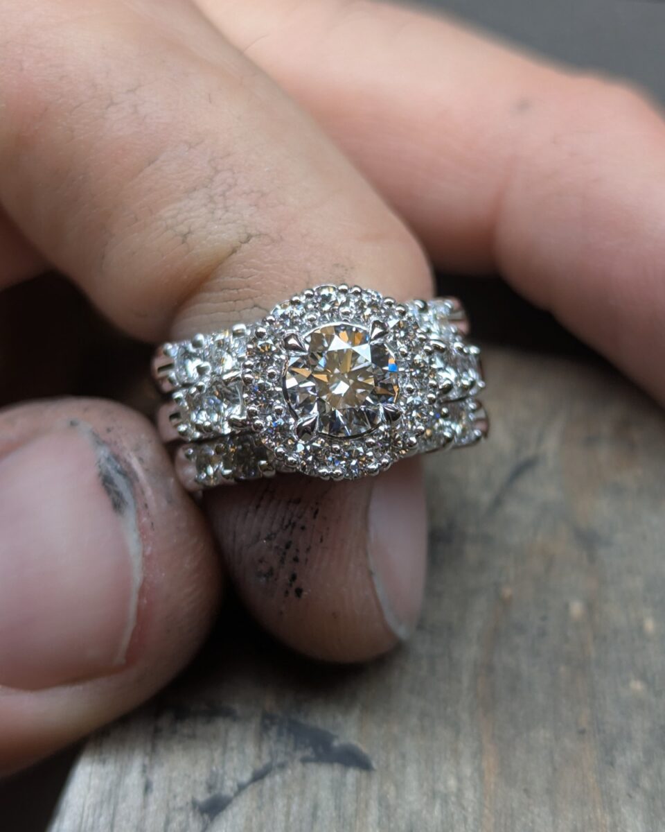 Finished custom wide white gold band with a round diamond centre in a pave halo flanked by diamond rows