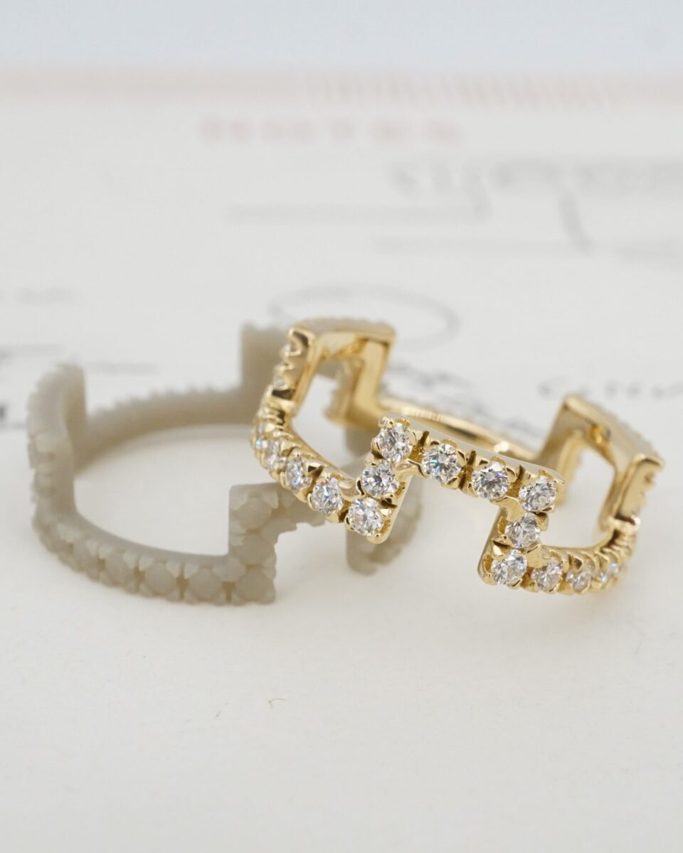 Finished yellow gold pave diamond geometric band beside its resin model on the original design drawing