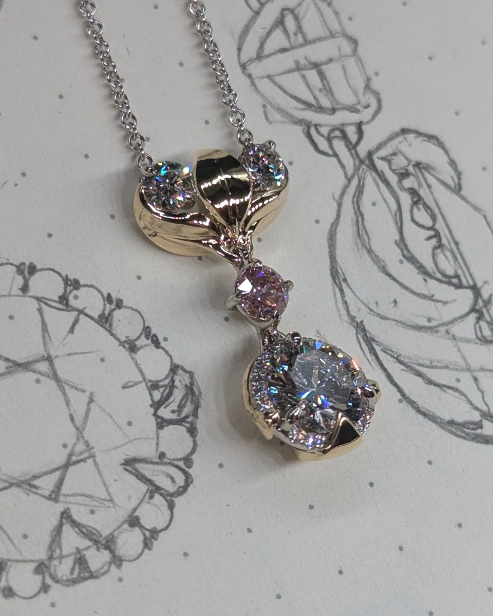 The finished custom diamond and gold pendant resting on the original hand-drawn design sketches