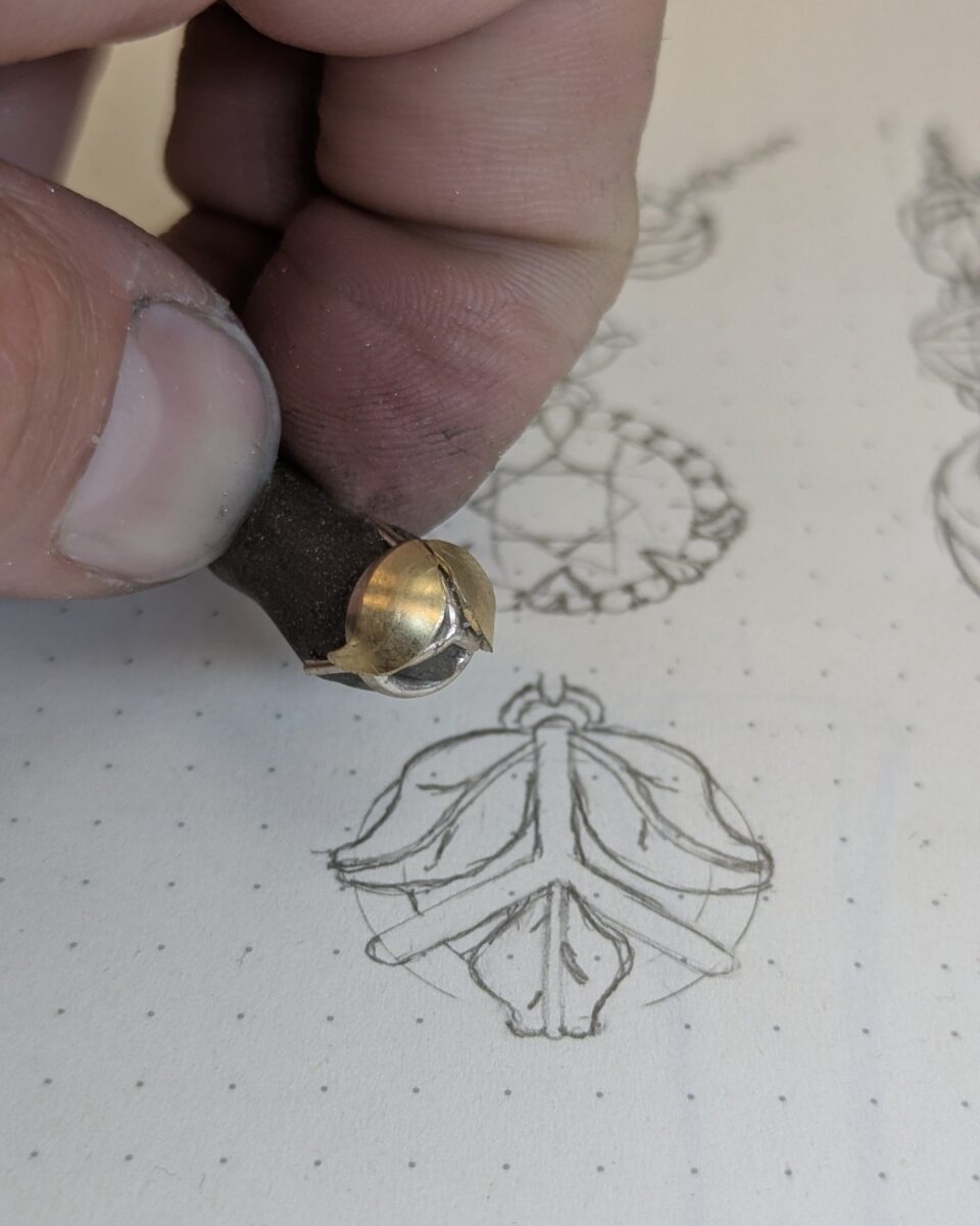 A part-built gold and silver setting held over the original design sketches midway through fabrication